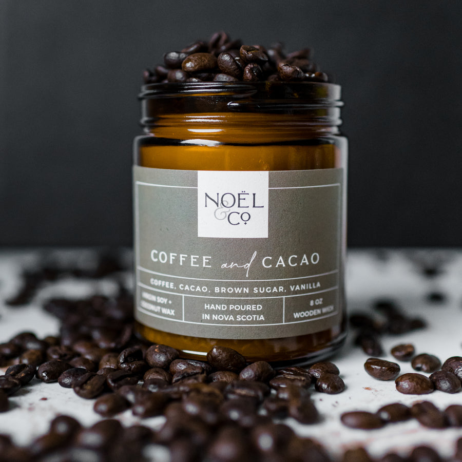 A candle in an amber glass jar and coffee beans on top and around it.
