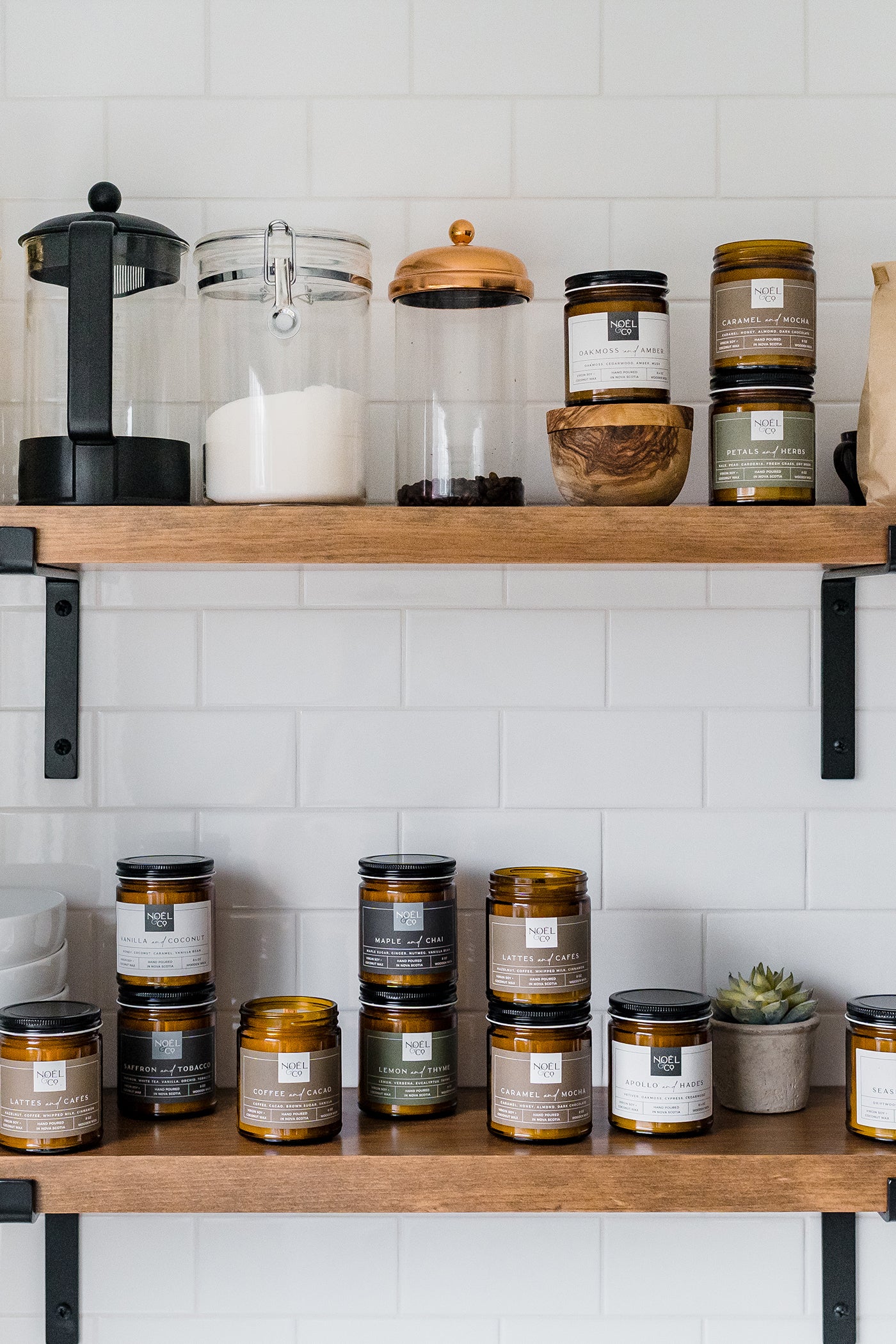Candles in amber glass jars on a shelf. Some with a black lid on and some without a lid.