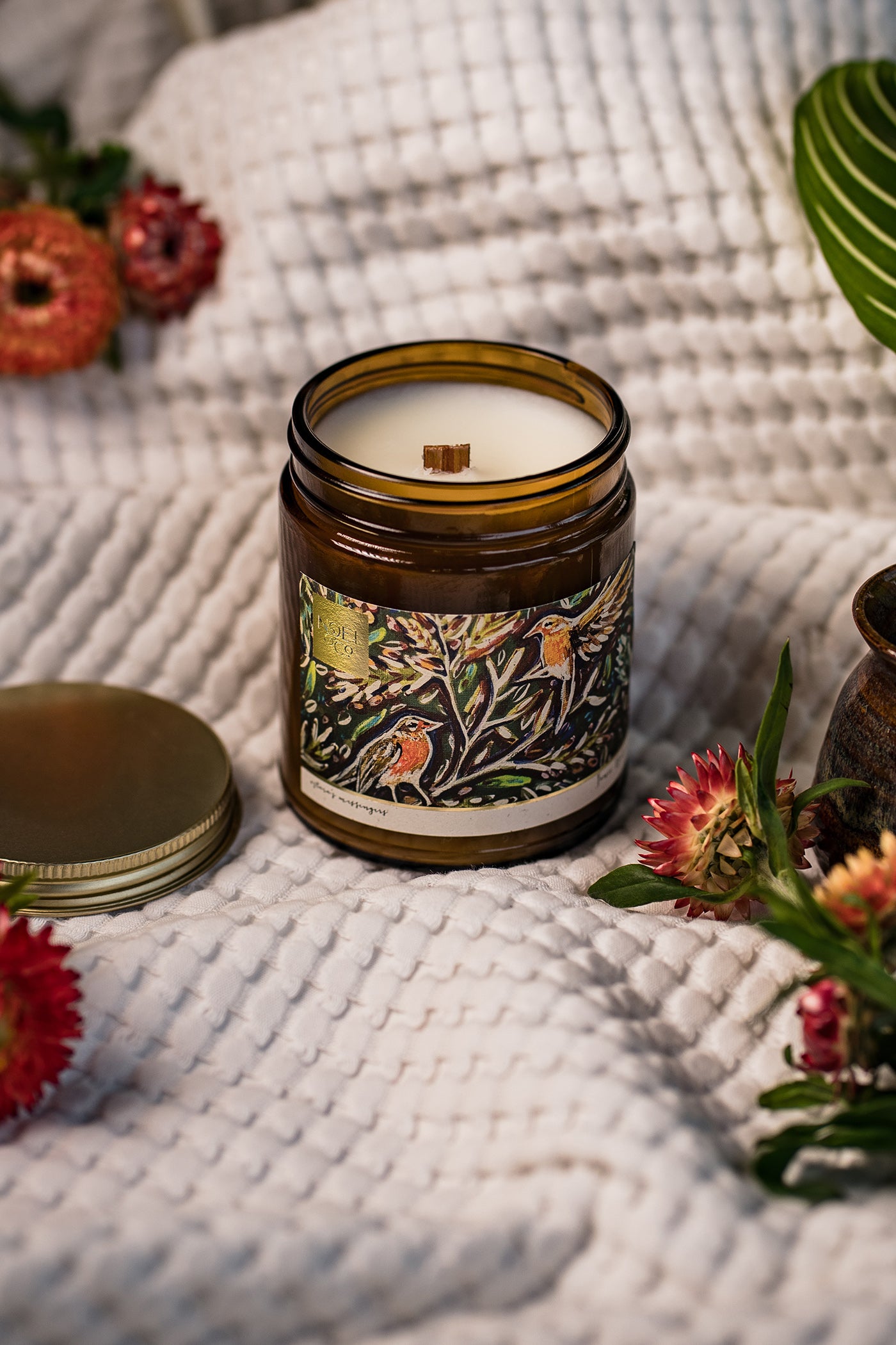 Decorative Noel & Co candle with a colourful label on a textured surface with robins.