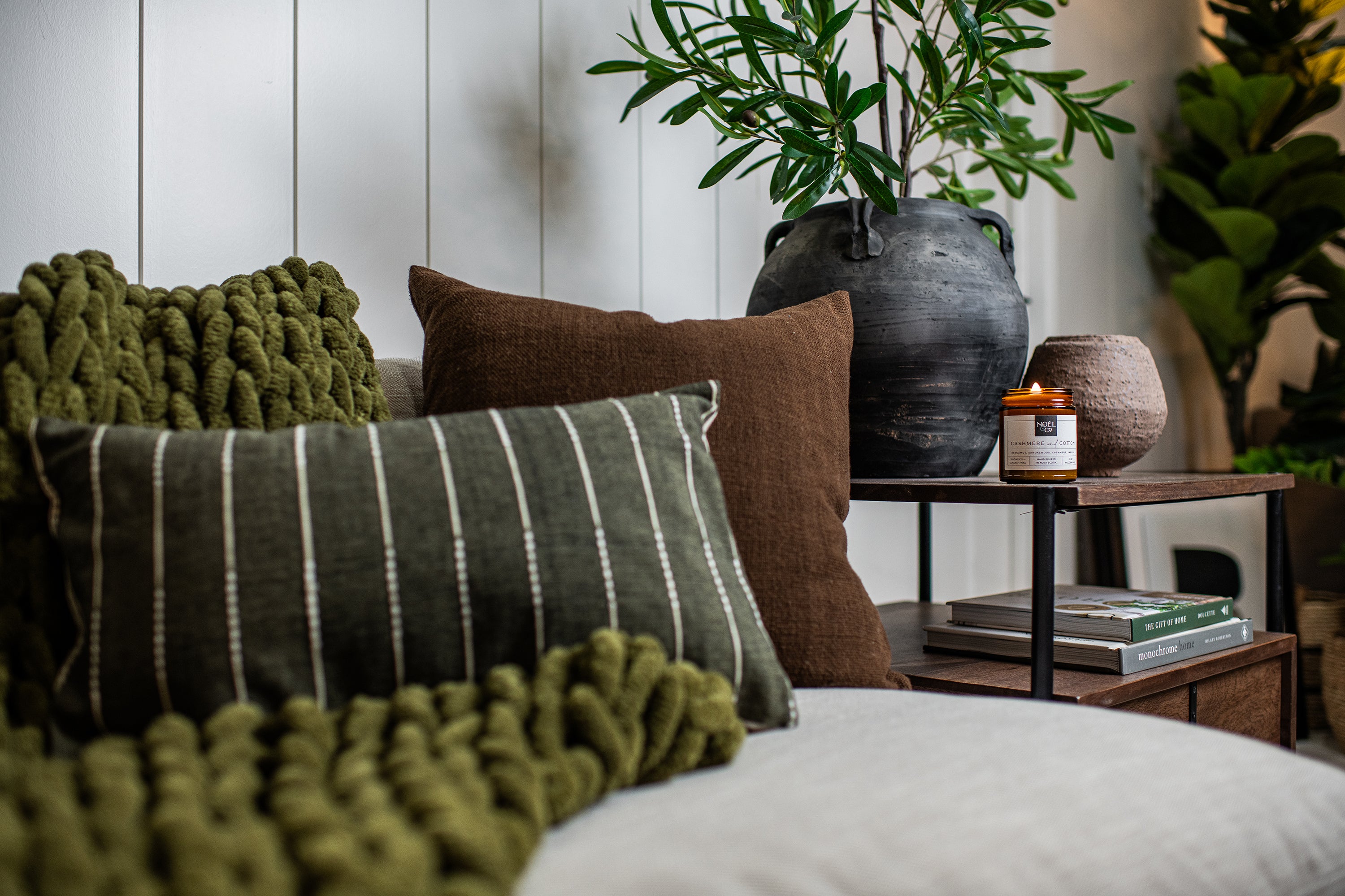 A lit candle in an amber glass jar on side table.