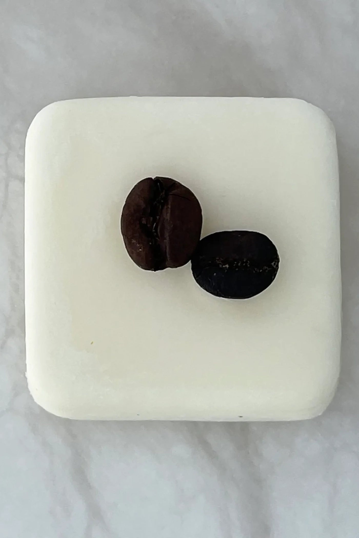 A single white wax melt with two coffee beans on top.