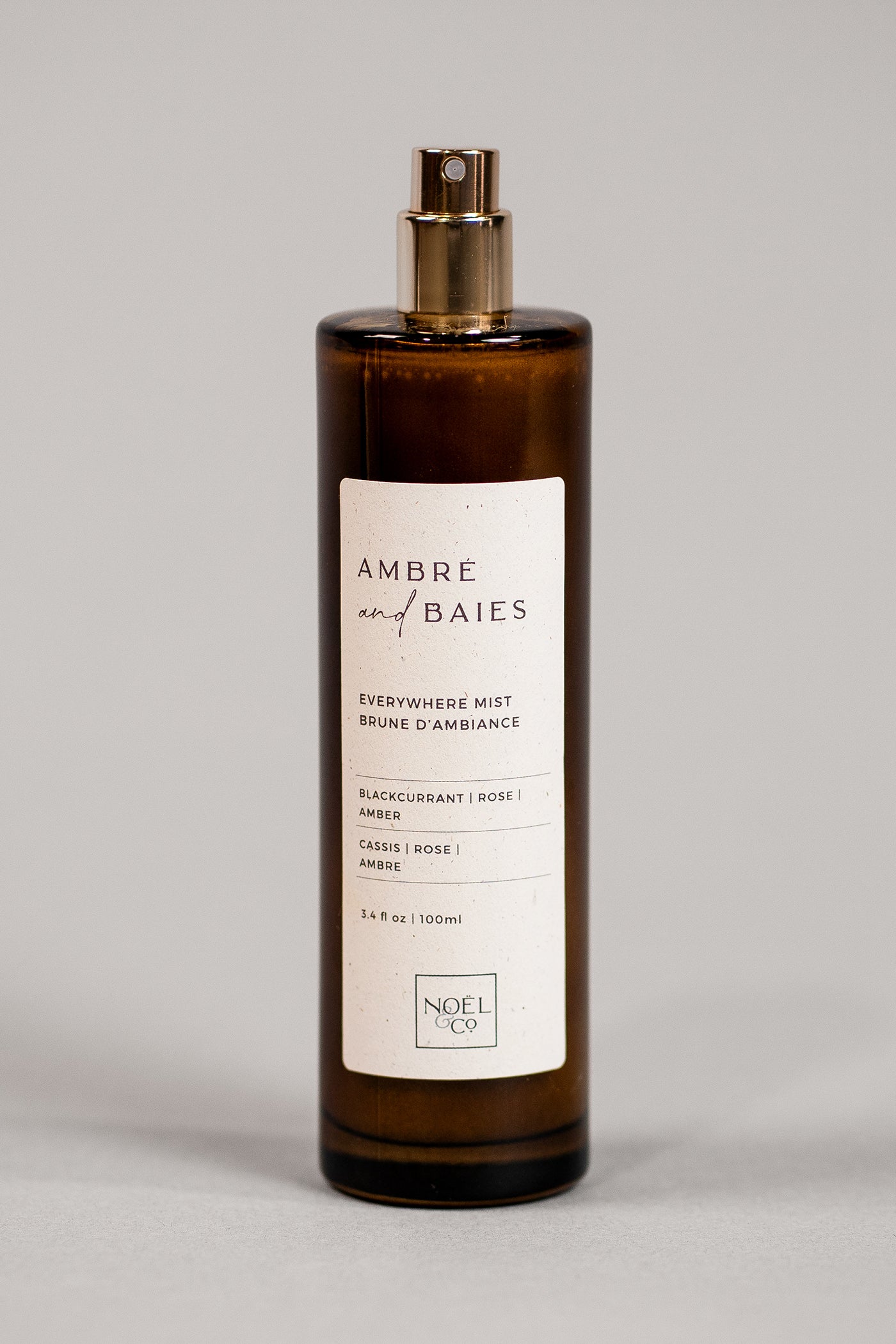 An amber glass Noel and Co everywhere mist with a gold-colored cap and label that reads 'Ambre & Baies'