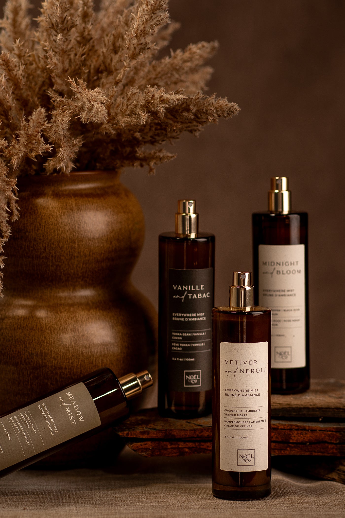 A selection of Noel and Co everywhere mist bottles, displayed in a rustic setting with dried flowers nearby.
