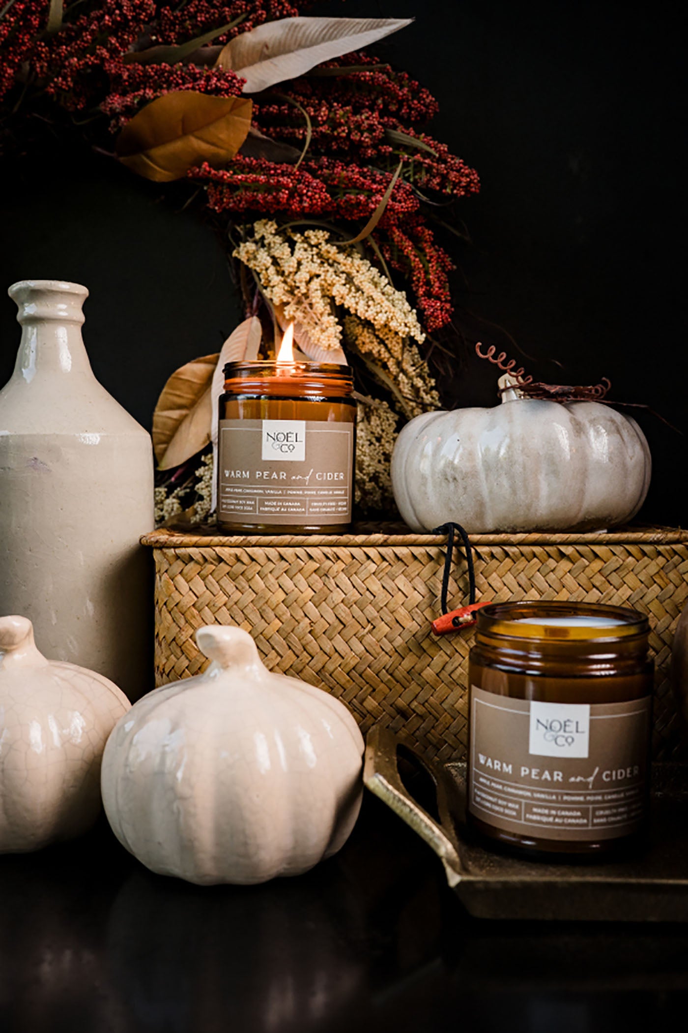 Noel and Co Warm Pear & Cider with decorative pumpkins and flowers on a dark surface