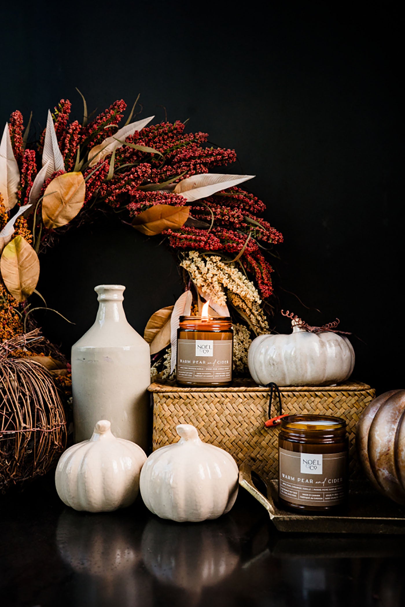 Autumn-themed decor with Noel and Co candles, pumpkins, and leaves on a dark background