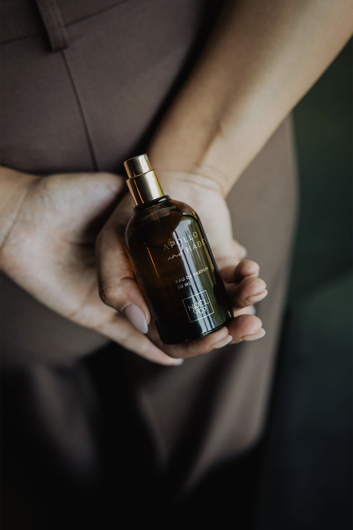 Hand holding a Noel and Co 50ml perfume  with a gold cap against a blurred background