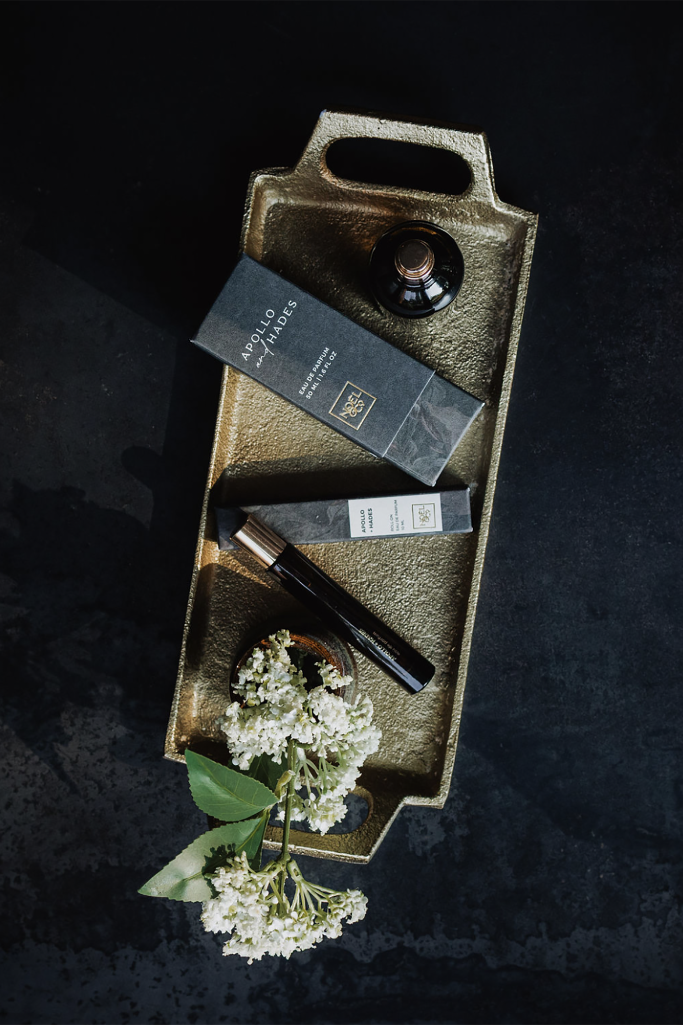 Decorative tray with Noel and Co Apollo and Hades perfume, and flowers on a dark background