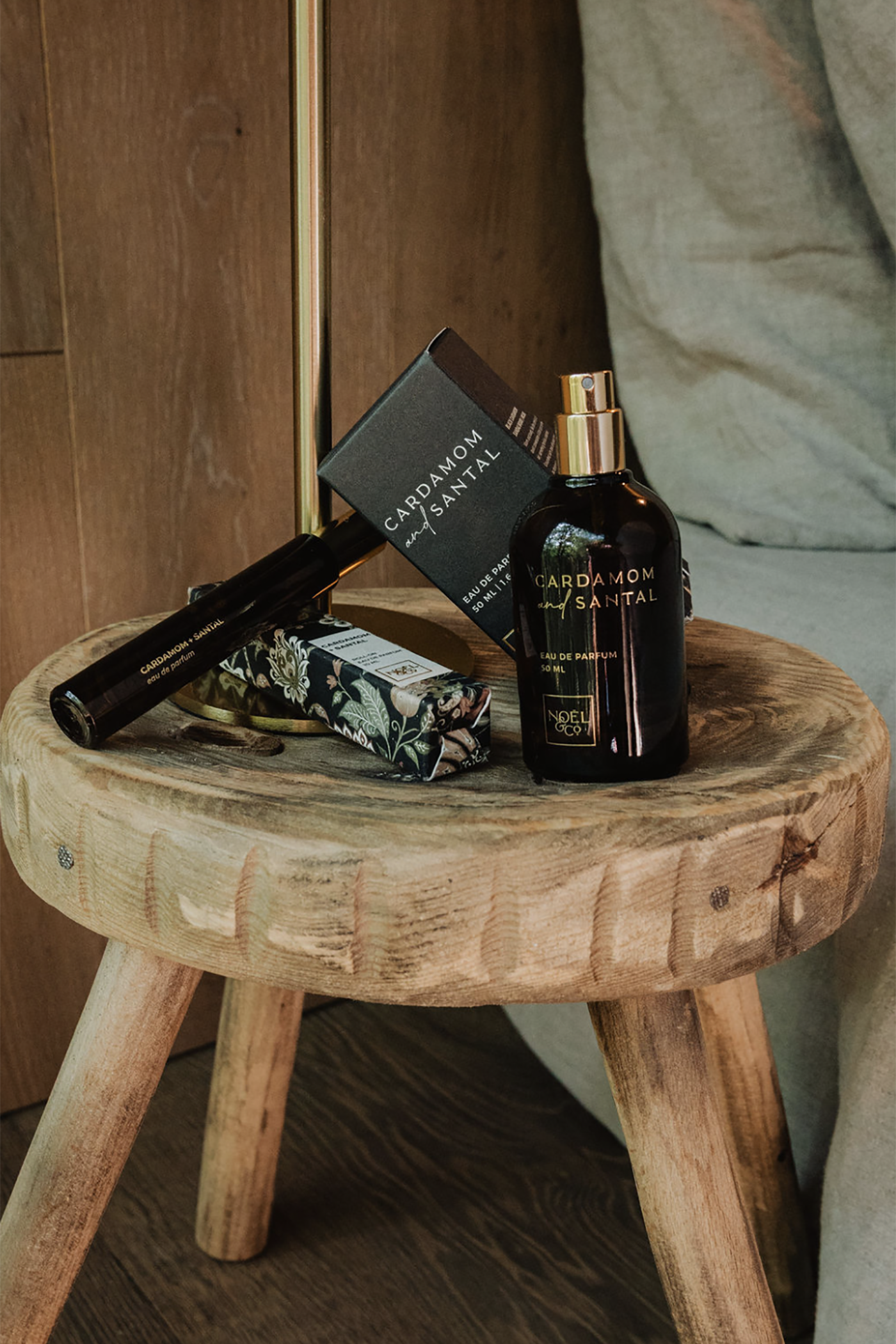 Noel  and Co large perfume and rollerball perfume on a wooden stool against a wooden wall.