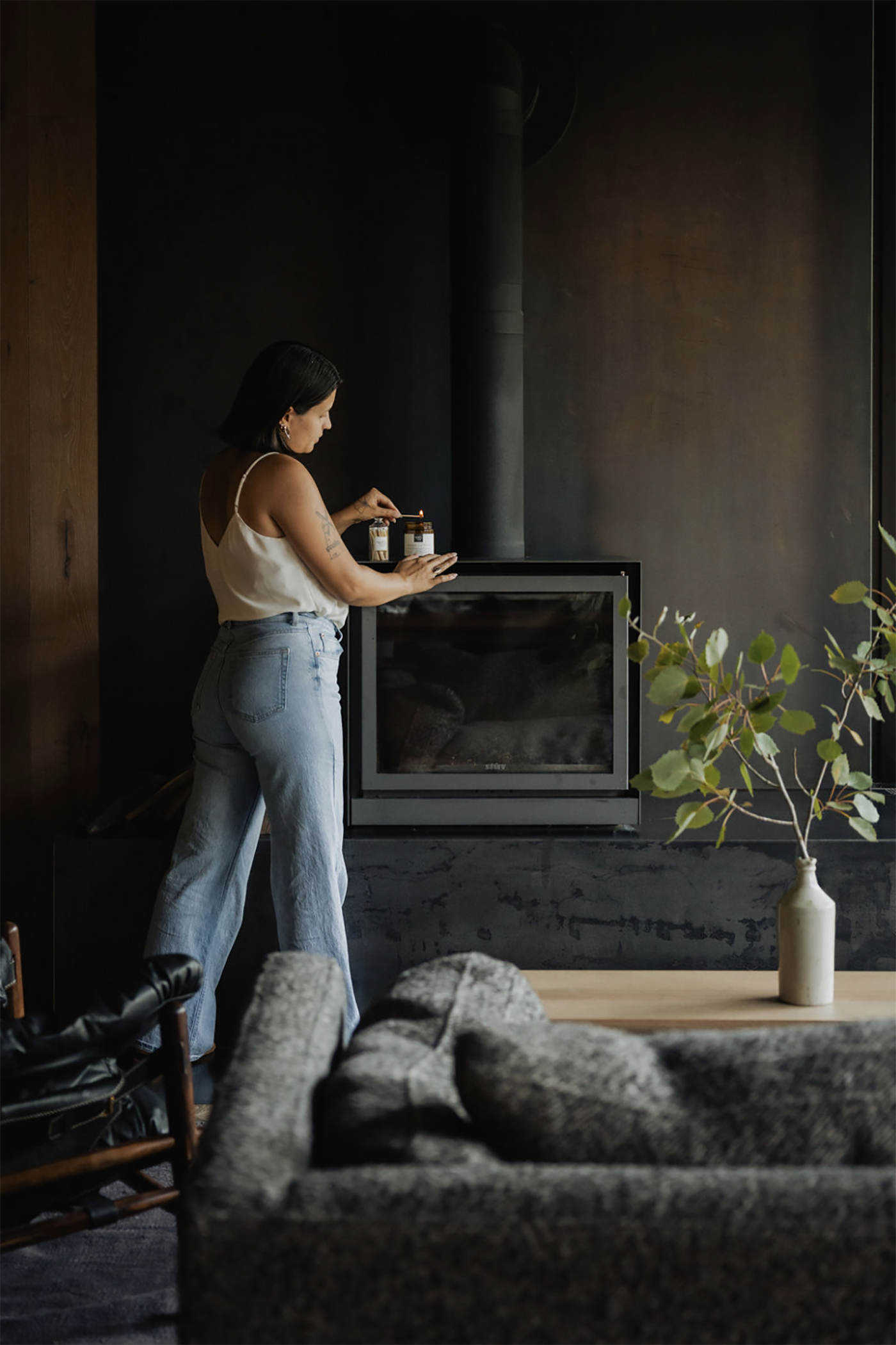 Woman standing in a dimly lit room with a Noel and Co candle and a plant.