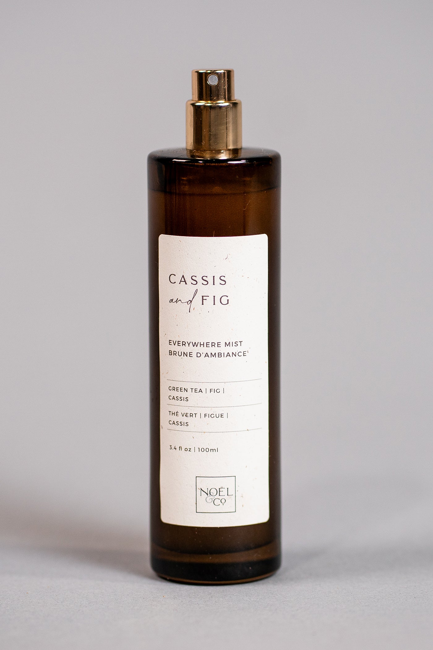 A bottle of Noel and Co Cassis & Fig everywhere mist with a label that includes the product name and a brief description. The bottle cap is gold-colored, and the background is plain.