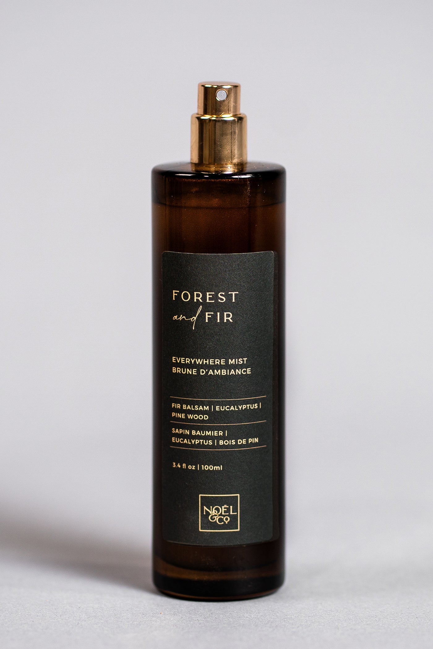 A Noel and Co bottle of Forest & Fir everywhere mist with a gold-colored cap, placed against a plain background.