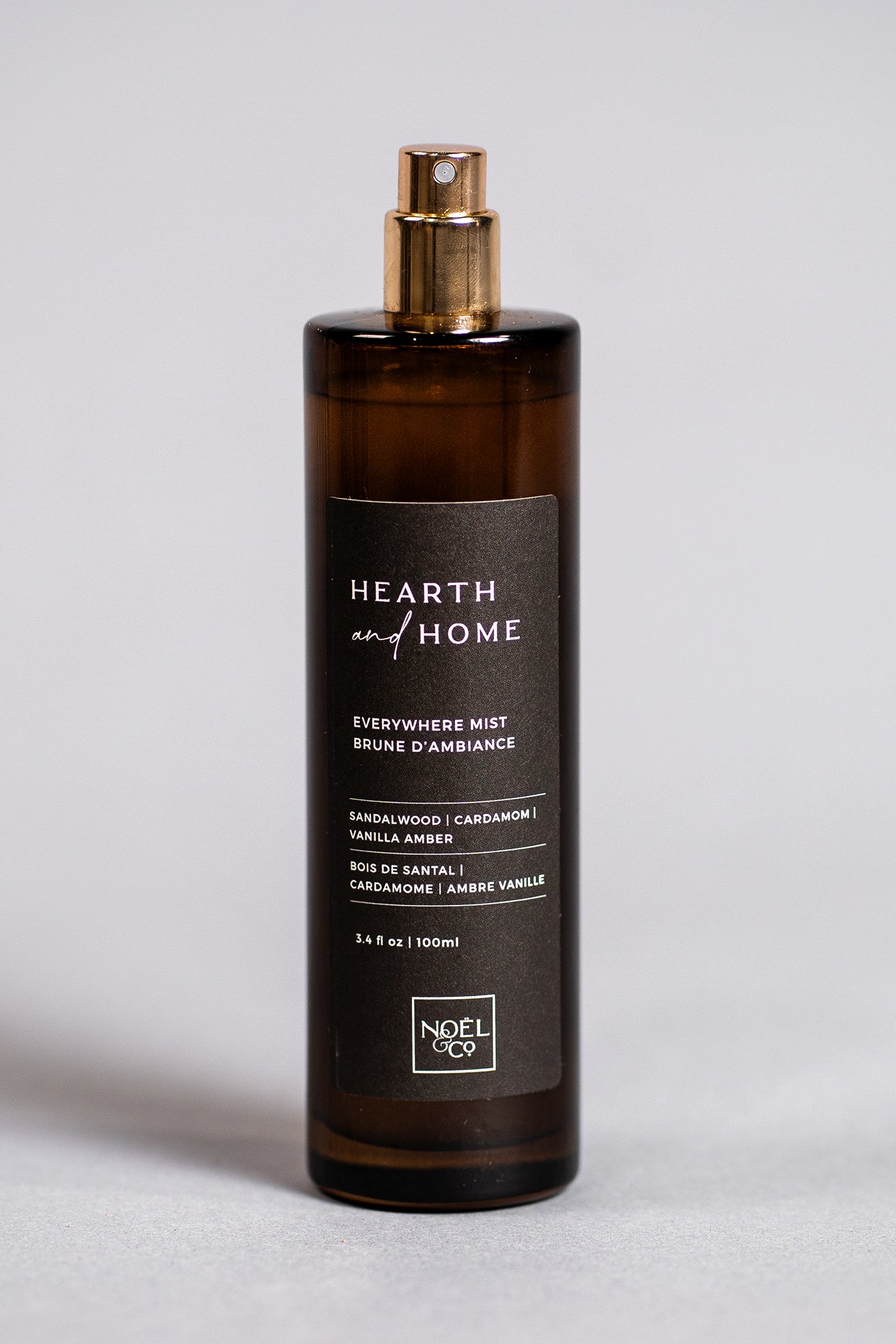 An amber glass Noel and Co everywhere mist bottle with a gold-colored cap and black label, labeled 'HEARTH & HOME'.