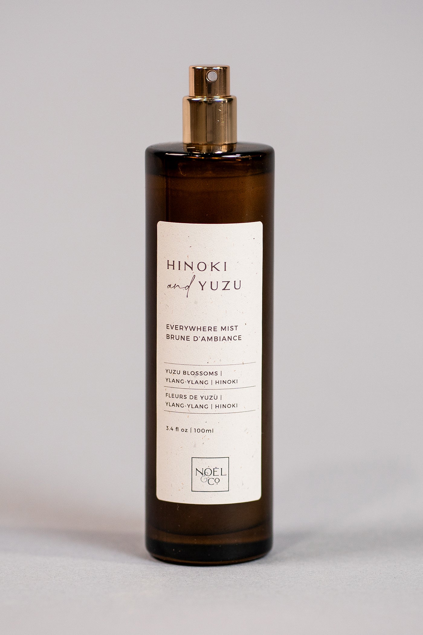 A tall, slender bottle of Hinoki & Yuzu everywhere mist with a cream label and a gold cap.