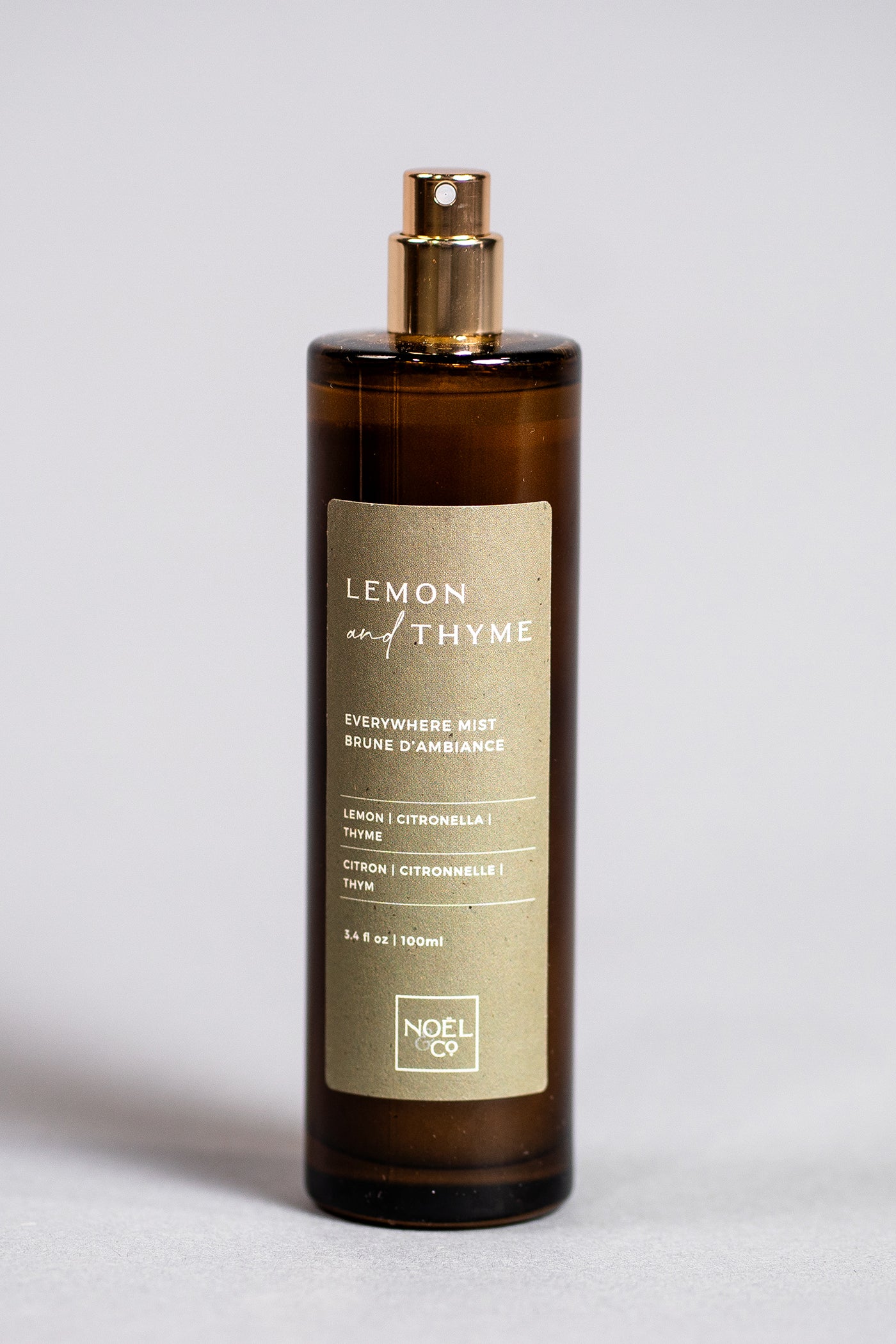A tall, slender bottle of Lemon & Thyme Noel and Co everywhere mist with a gold cap and a label that includes the product name and other details.