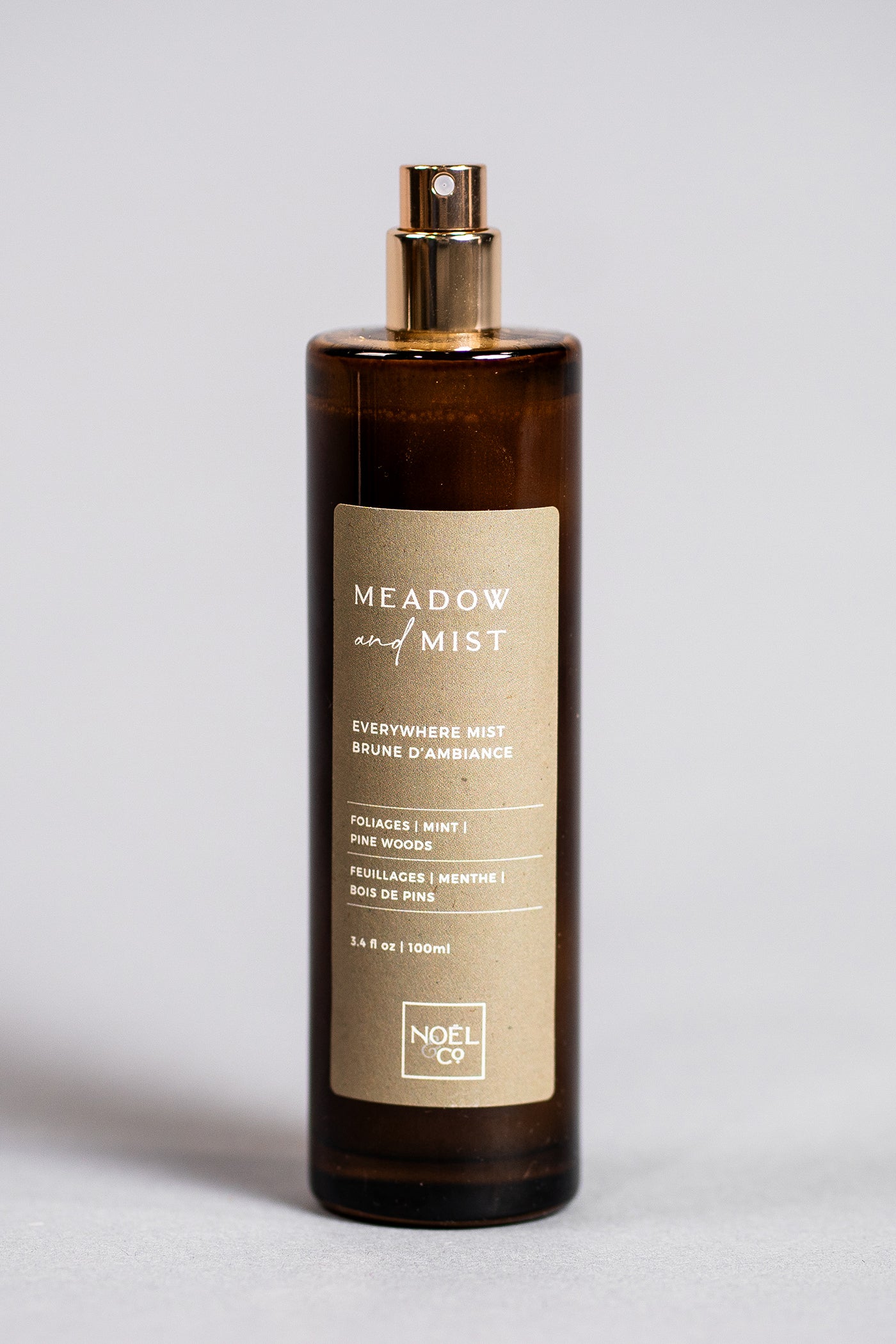 A bottle of 'Meadow & Mist' fragrance by noël & co. with an amber glass and a gold-colored cap and label.
