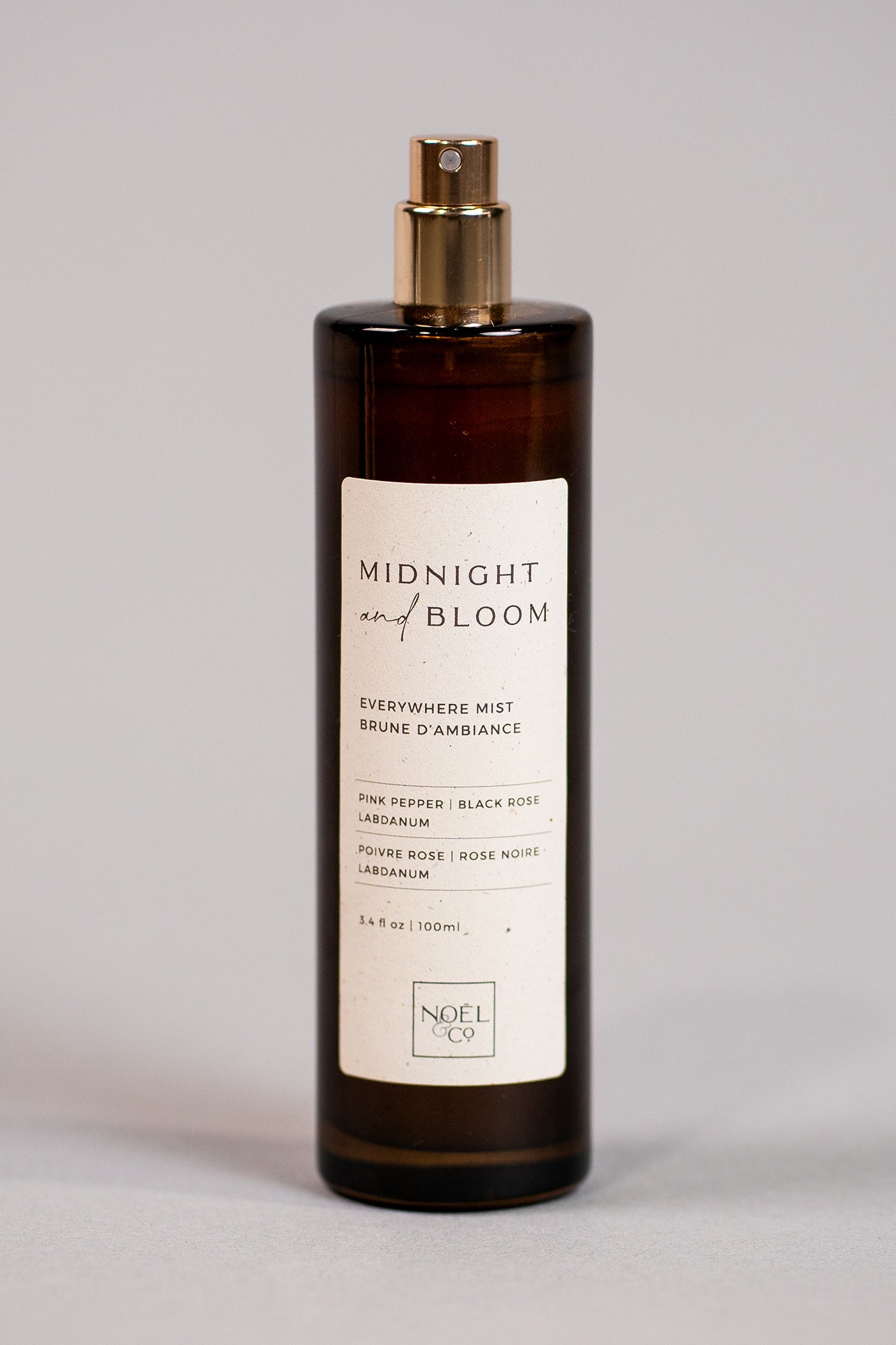An amber glass everywhere mist bottle with a gold cap labeled 'MIDNIGHT & BLOOM', containing 100ml