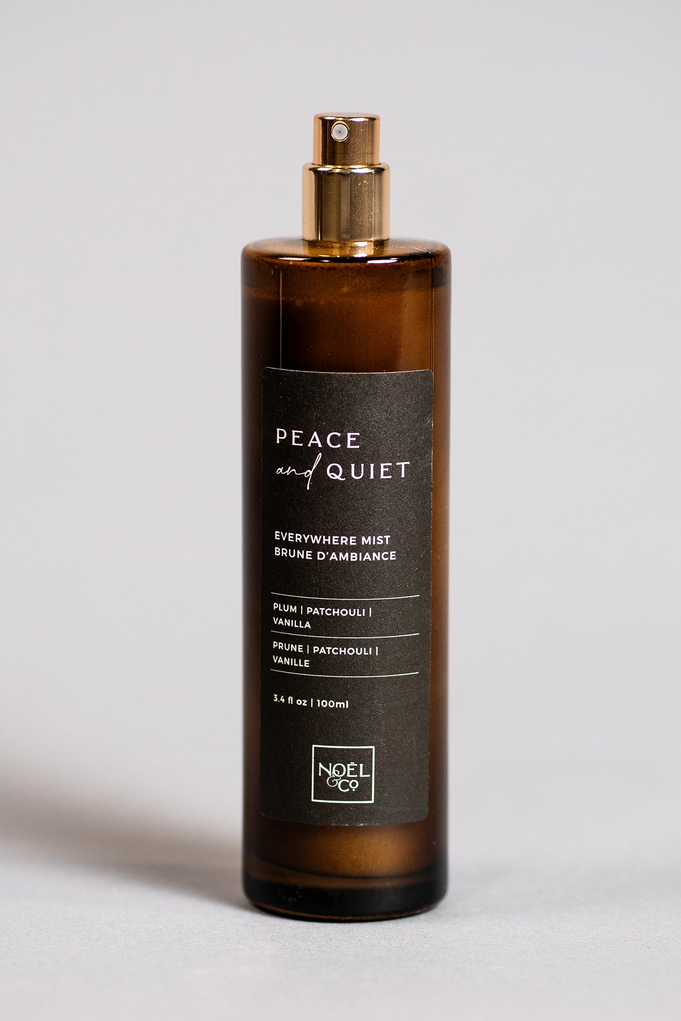 An amber glass Noel and Co everywhere mist with a gold cap labeled 'PEACE & QUIET'.