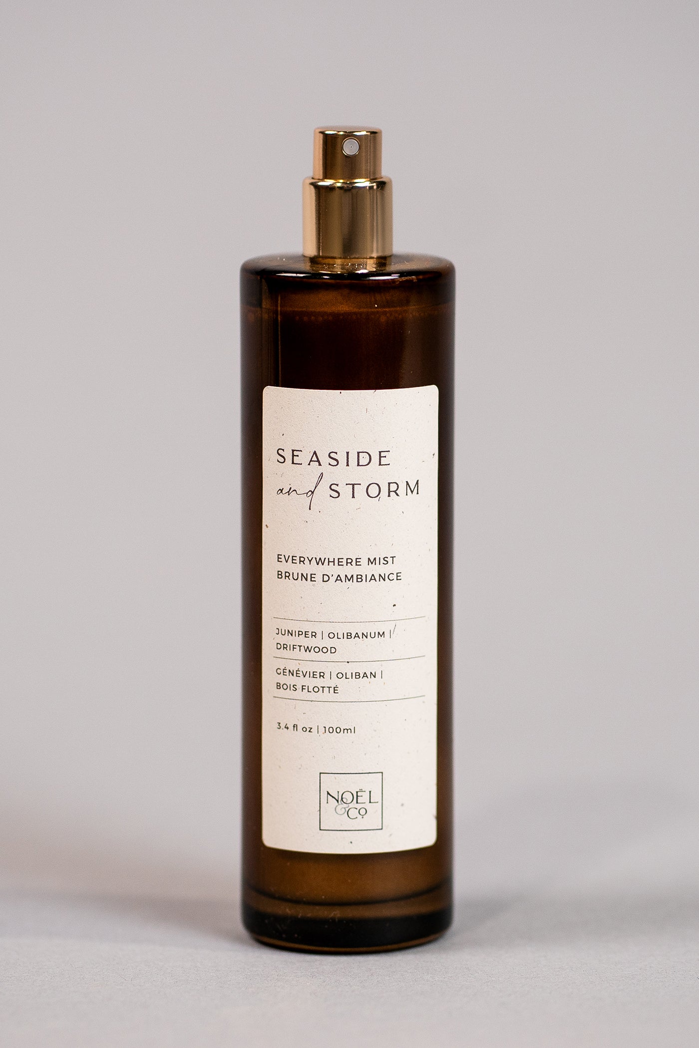 A tall, slender bottle with a gold-colored cap, labeled 'Seaside & Storm' by Noël and Co, containing everywhere mist.