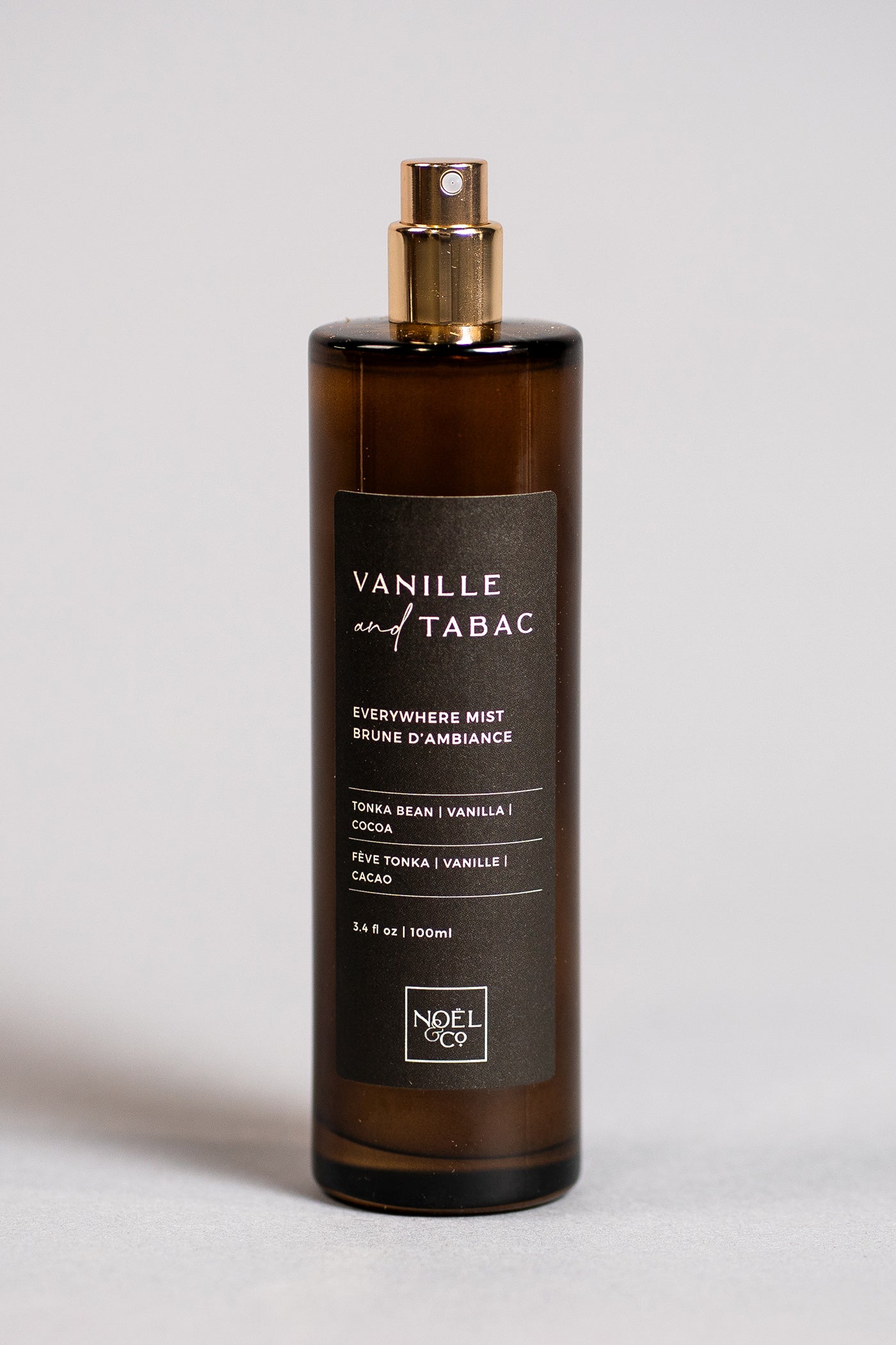 An amber glass everywhere mist bottle with a gold-colored cap and label that reads 'Vanille Tabac' with additional text describing the fragrance's notes.
