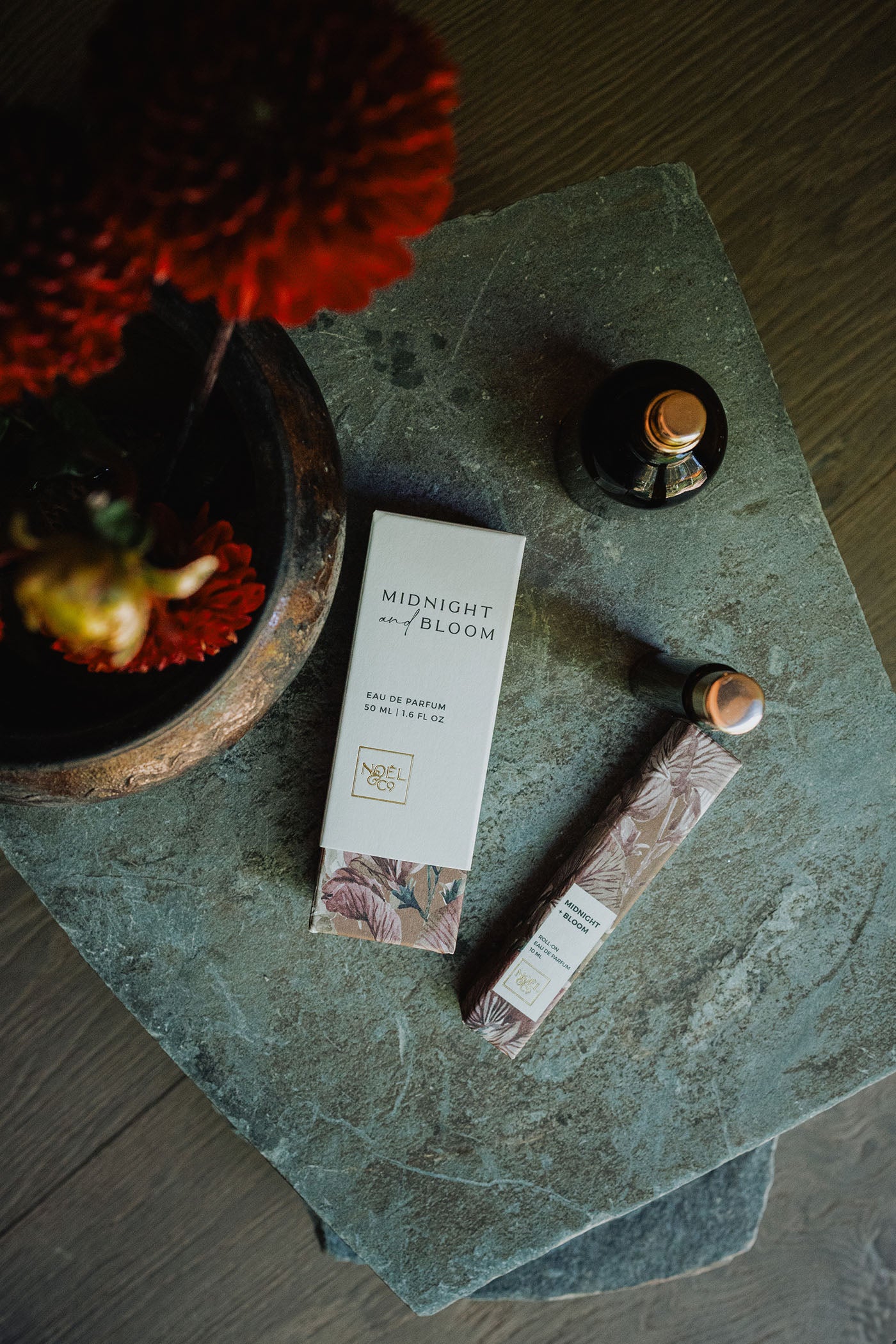 Noel and Co Midnight and Bloom perfume on a stone surface with a decorative plant.