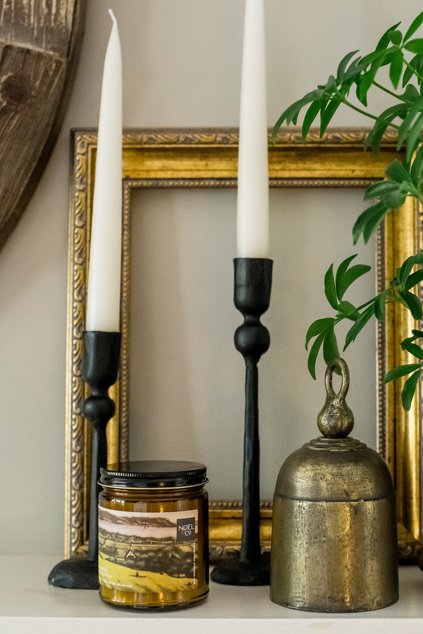 A scented Noel and Co candle depicting Grand Pre Nova Scotia, placed on a shelf alongside a picture frame and other decorative items.