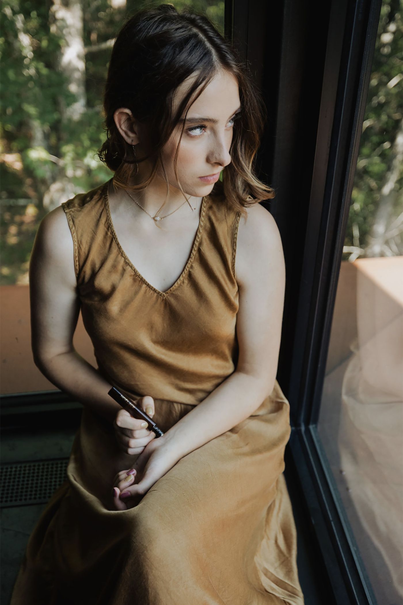 Woman in a gold dress sitting by a window with a Noel and Co rollerball perfume in her hand.