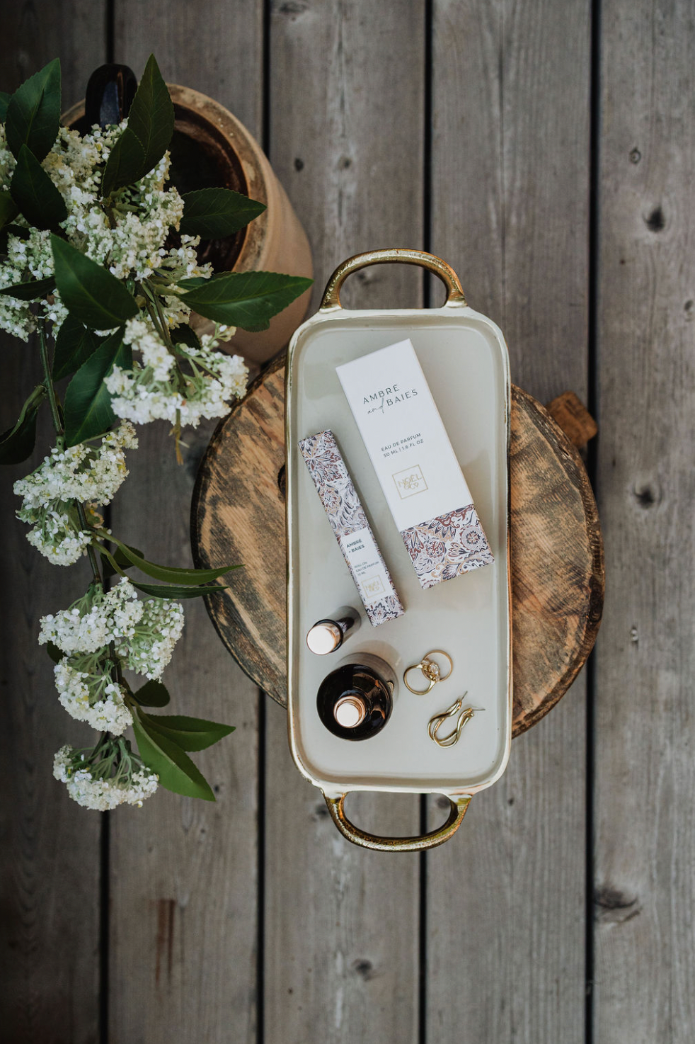 Tray with Noel and Co Ambre and Baies perfume on a wooden surface with flowers
