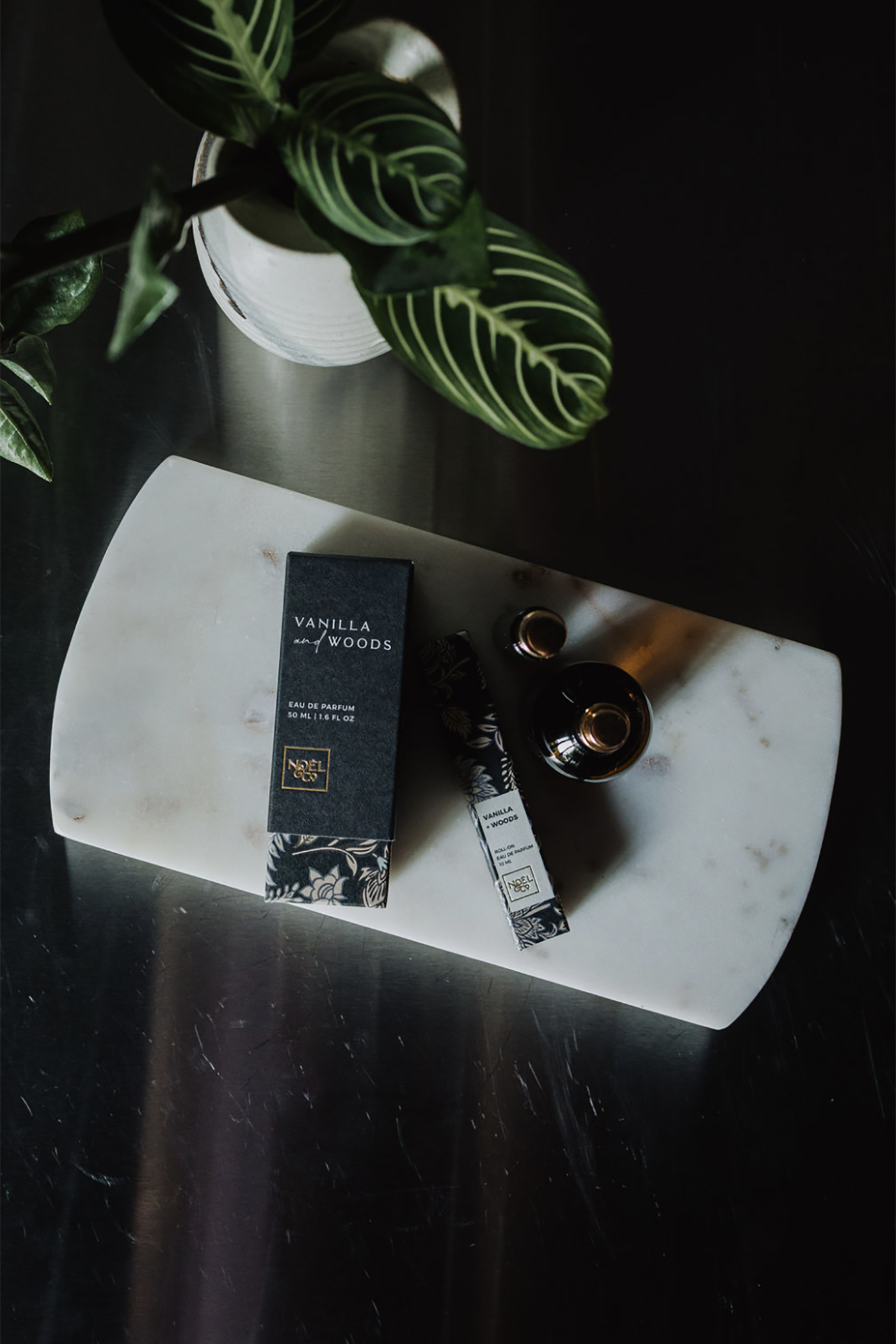 Vanilla Woods product packaging on a marble surface with a plant in the background