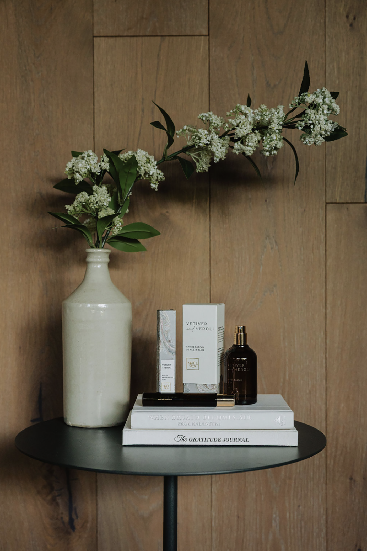 Decorative setup with Noel and Co Vetiver and Neroli perfume on a small round table against a wooden wall.