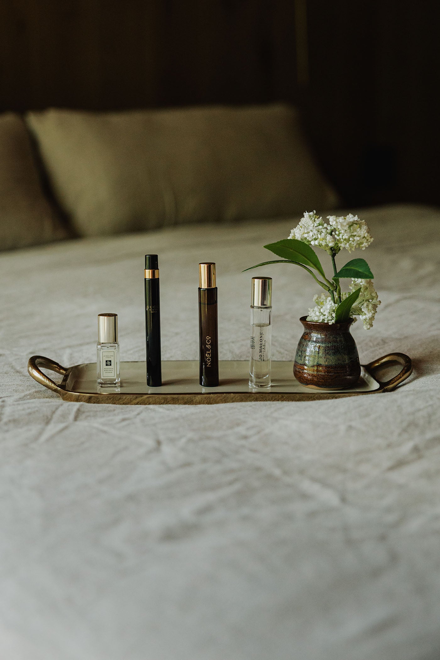 Set of perfume bottles on a tray with a small vase of flowers on a bed.