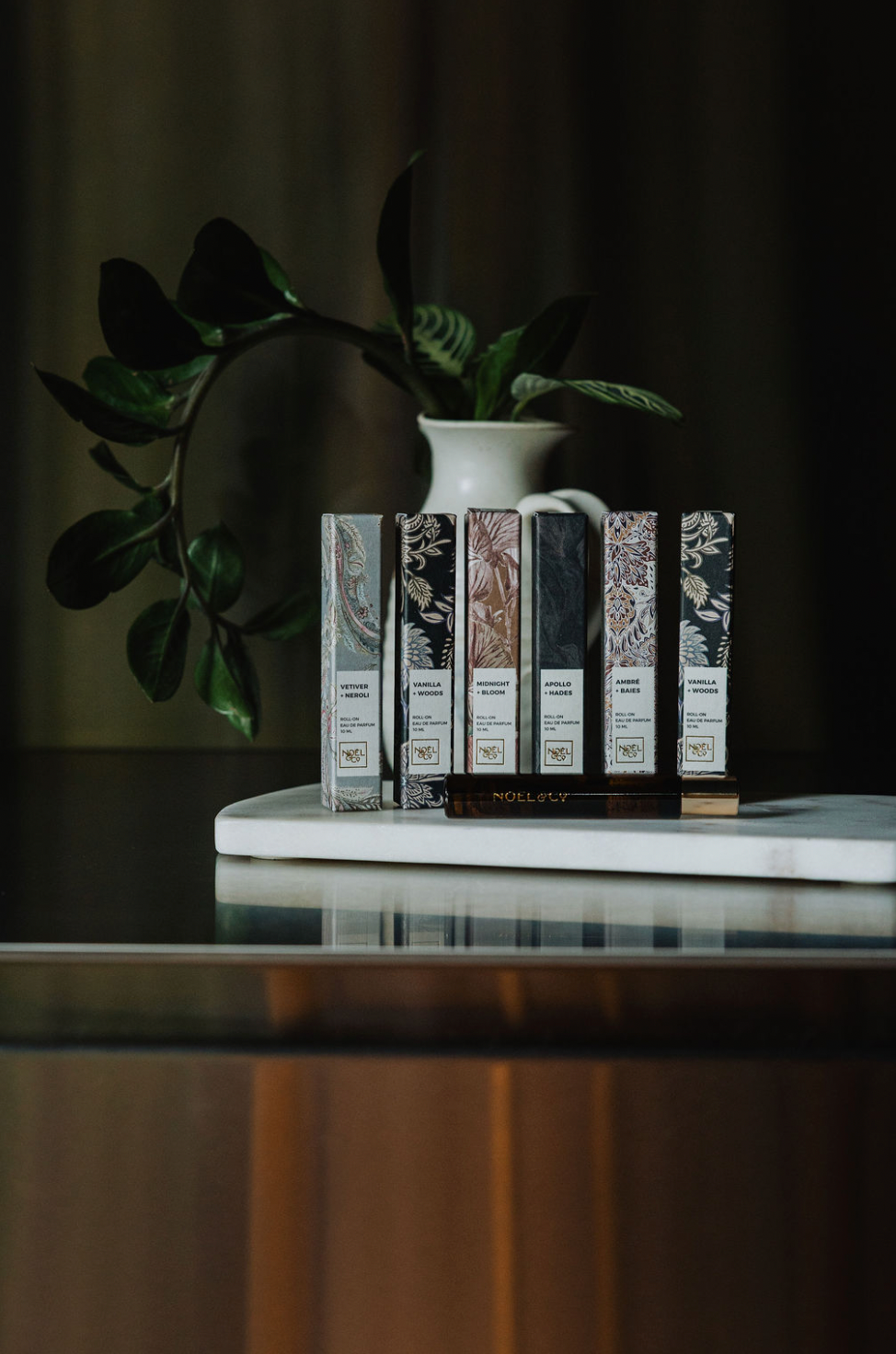 Set of 6 Noel and Co rollerball perfumes,  on a marble surface with a plant in the background