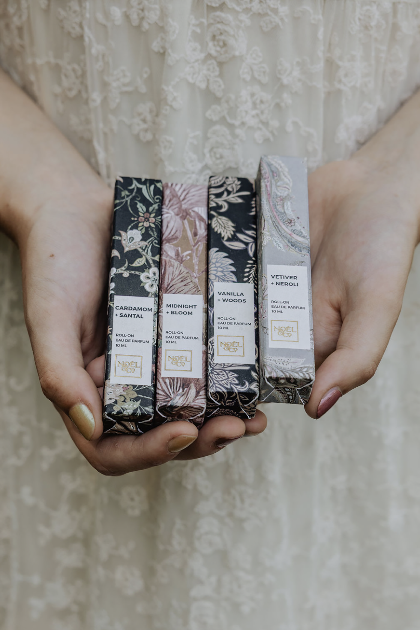 Four Noel and Co rollerball perfumes held in hands against a neutral background