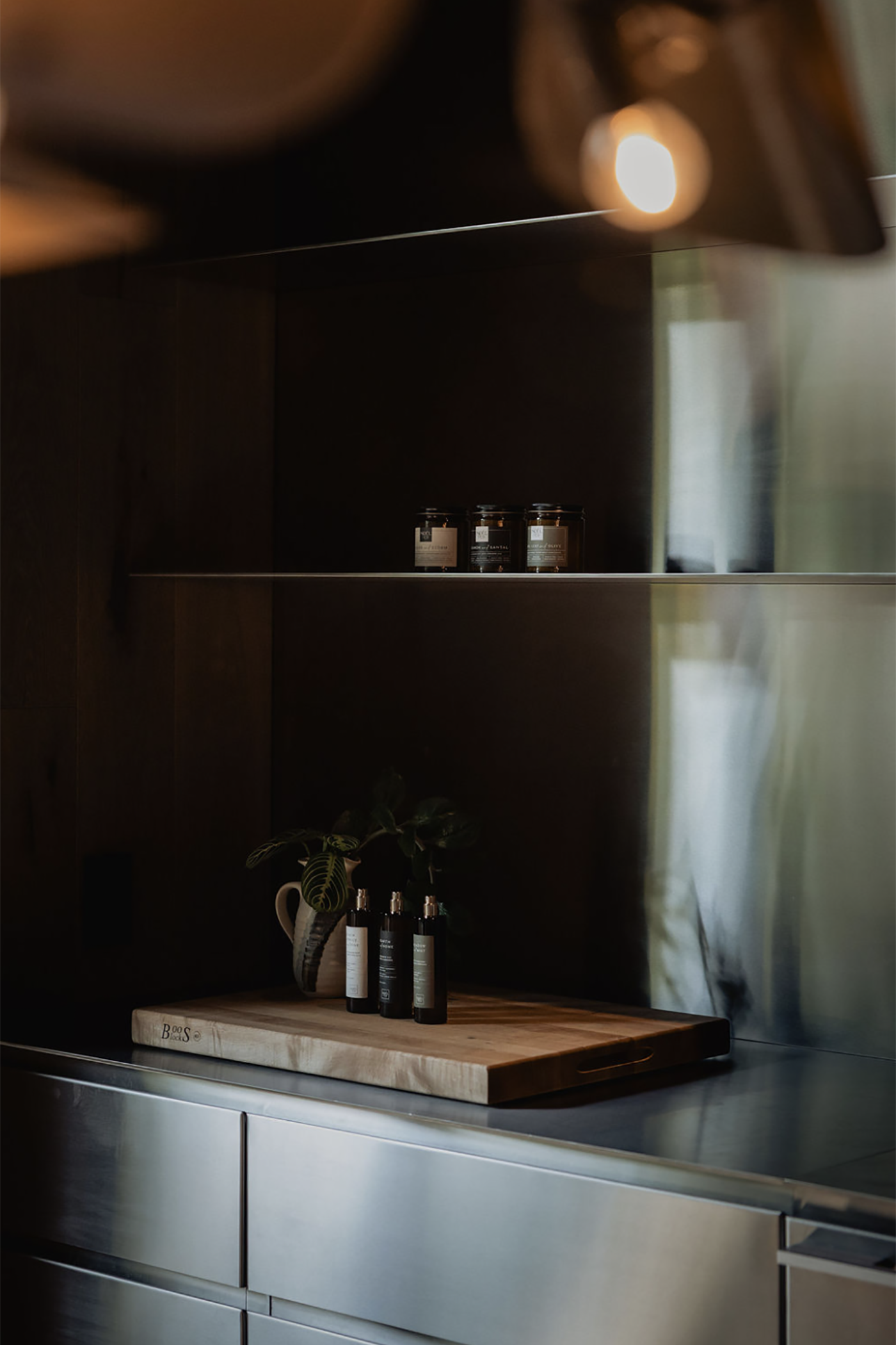 Modern kitchen with stainless steel appliances and a cutting board with bottles on a dark countertop.